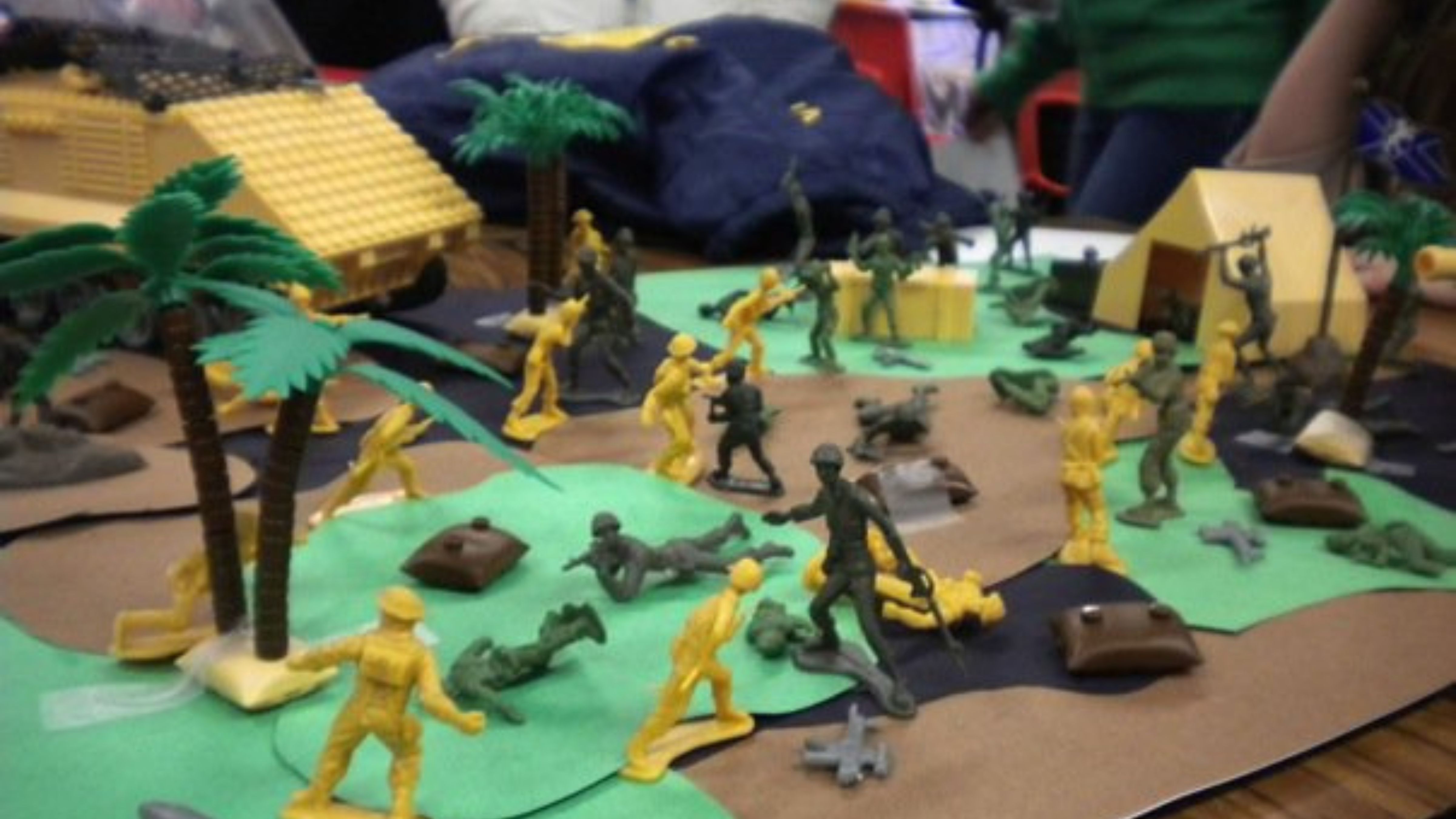 School diarama with green army men on a table decorated to look like a battle field. 