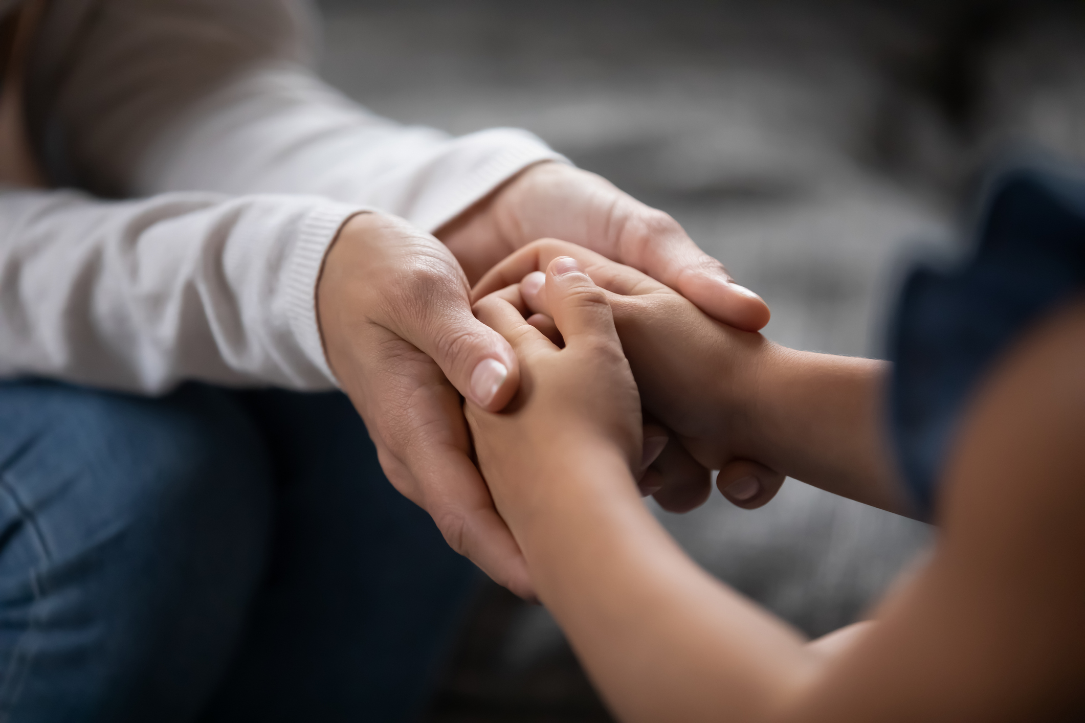 Two sets of hands; an adult holding a child's hands in both of their own.