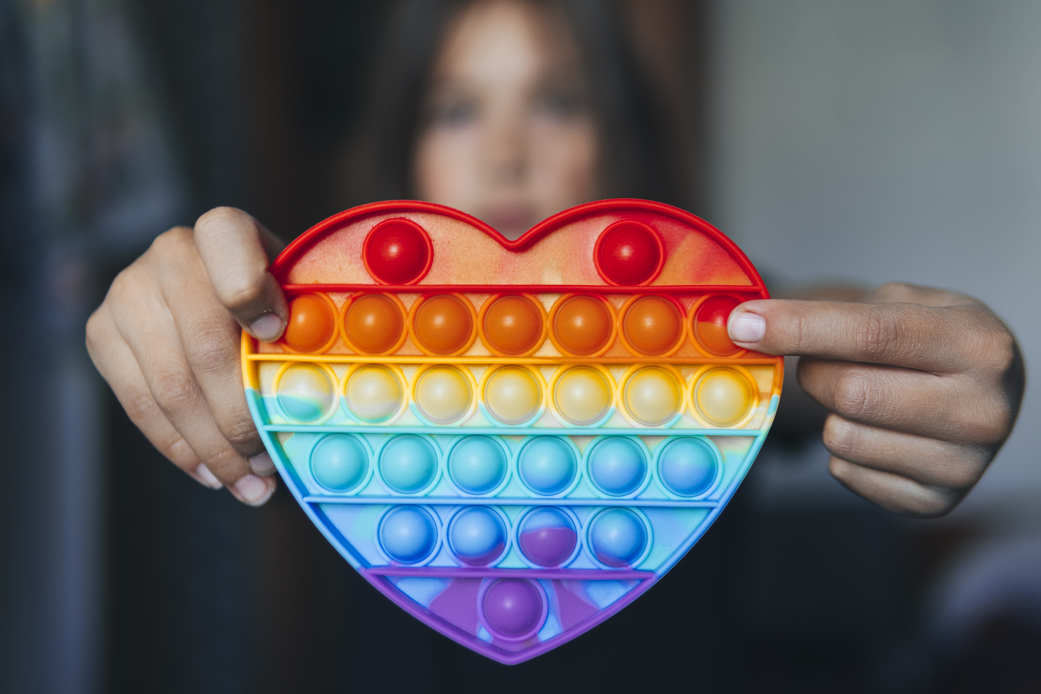 A person holding a plastic, rainbow, heart-shaped sensory toy. 