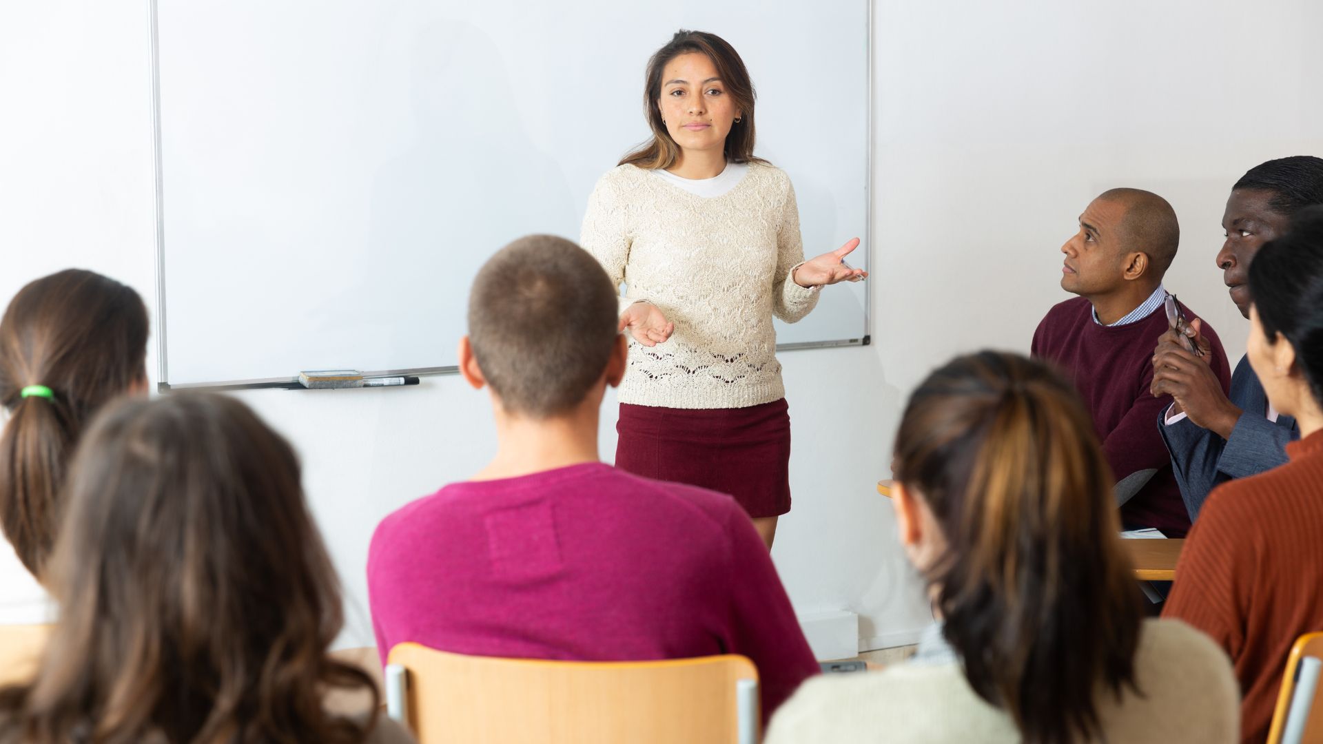 One adult woman stands in front of a small crowd of seated people.